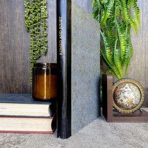 May include: A black and blue hardcover book titled "Romeo and Juliet" is stacked on top of two other books. A clear glass jar with a brown lid sits on top of the books. A small globe sits on a wooden bookend.