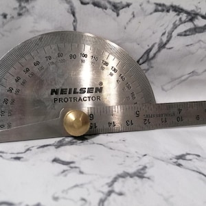 May include: A silver protractor with a brass knob and a ruler marked in inches. The protractor is labeled "NEILSEN PROTRACTOR".