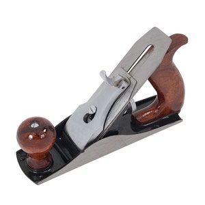 Peut inclure: Un rabot à main noir et argent avec une poignée en bois. Le rabot a une lame en métal et un bouton en bois.