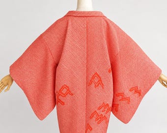 May include: A coral-colored textured jacket with wide sleeves and a folded collar. The garment features a repeating pattern of embroidered orange geometric shapes resembling stylized birds or chevrons scattered across the back and sleeves.
