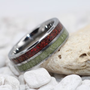 May include: A silver ring with a green and red inlay. The ring is on a white background.