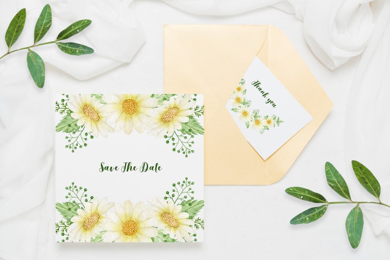 May include: A white card with a floral border and the text "Save The Date" in green script. A smaller white card with a floral border and the text "Thank you" is on top of a gold envelope.