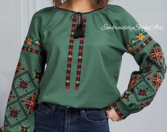 May include: Green long-sleeved blouse with detailed floral embroidery in red, yellow, and black on the sleeves and bodice. The blouse has a round neckline with a tassel tie and the text "Embroidery Style Art".