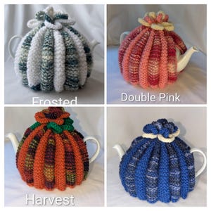 May include: Four knitted tea cosies in different colours, including white, pink, orange, and blue, each covering a white teapot. The cosies are labelled "Frosted", "Double Pink", "Harvest", and "Blue".