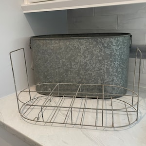May include: A galvanized metal tub with a wire bottle rack. The tub is oval shaped and has a distressed finish. The rack is made of wire and has a circular shape.