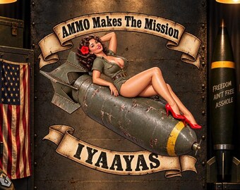 May include: A pin-up style poster featuring a person in a green military-inspired outfit reclining on a large olive-drab bomb. The text reads AMMO Makes The Mission and IYAAYAS. A separate missile on the right displays the text FREEDOM AIN'T FREE ASSHOLE.
