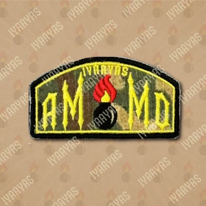 May include: A yellow and black embroidered patch with the text "IYAAYAS AMMO" in a gothic font. A black bomb with a red flame is in the center of the patch.