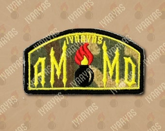 Op de afbeelding: Een geborduurde patch in geel en zwart met de tekst "IYAAYAS AMMO" in gotische letter. In het midden van de patch bevindt zich een zwarte bom met een rode vlam.