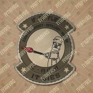 May include: A circular patch with a cartoon robot holding a lit rocket. The patch has text that reads "IF IT FLIES, ROCKET-ARTILLERY-MORTAR, IT DIES." The patch is primarily olive green and gray.