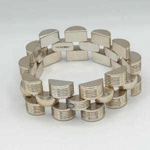 May include: Silver-toned bracelet with a geometric design. The bracelet is composed of semi-circular and rectangular links, creating a unique, articulated pattern. The links are connected to form a flexible band. The bracelet is made in China.