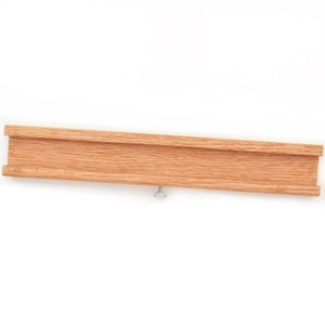 May include: A wooden track piece with a groove in the center, designed for use with a toy train set. The track piece is made of natural wood and has a light brown color. A small silver screw is visible on the bottom of the track piece.