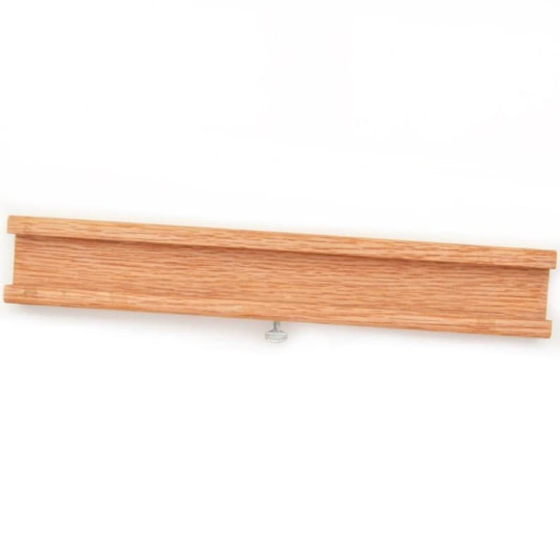 May include: A wooden track piece with a groove in the center, designed for use with a toy train set. The track piece is made of natural wood and has a light brown color. A small silver screw is visible on the bottom of the track piece.