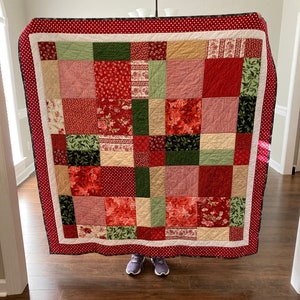 May include: A red, green, and white patchwork quilt with a floral pattern. The quilt is made of squares and rectangles of different sizes and colors.