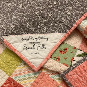 May include: A grey and white floral quilt with a label that reads "Snuggle Bug Stitching Handmade by Sarah Fulks Huntsville AL."
