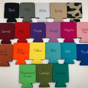 Op de afbeelding: Een verzameling van 18 verschillende gekleurde blikjeskoelers, elk met een andere kleur en naam die op de voorkant is gedrukt. De kleuren omvatten zwart, leisteen, wit, jute, camouflage, granaat, rood, paars, orchidee, magenta, pastelroze, gebrande oranje, oranje, geel, mint, jade, koninklijk, fluorescerend groen, kantine en smaragd.