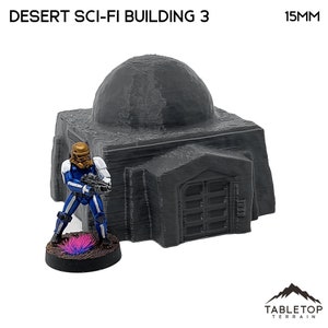 Pu&ograve; includere: Modello grigio di Desert Sci-Fi Building 3 con tetto a cupola e base rettangolare. Una figura in miniatura con armatura blu e bianca e casco dorato &egrave; nelle vicinanze. Il modello &egrave; di 15 mm.