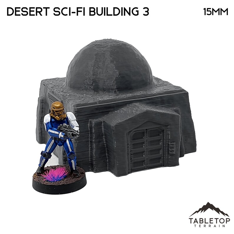 Pu&ograve; includere: Modello grigio di Desert Sci-Fi Building 3 con tetto a cupola e base rettangolare. Una figura in miniatura con armatura blu e bianca e casco dorato &egrave; nelle vicinanze. Il modello &egrave; di 15 mm.