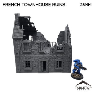 Puede incluir: Un modelo de plástico gris de una casa adosada francesa en ruinas a escala 28 mm. El edificio está parcialmente derrumbado, con mampostería visible y un techo roto. El modelo es adecuado para su uso en juegos de guerra de mesa o dioramas.