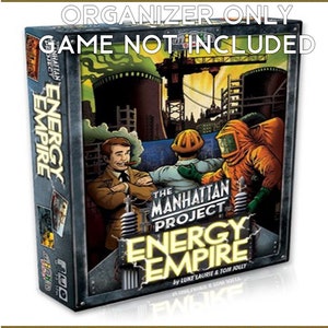 May include: The Manhattan Project: Energy Empire board game box art features a cartoon illustration of a city skyline with industrial buildings, a crane, and two men in hazmat suits. The text "The Manhattan Project: Energy Empire" is printed in large, bold letters on the box.