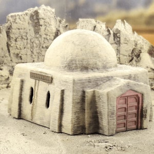 Pu&ograve; includere: Un edificio beige in miniatura con tetto a cupola e porta rossa. L'edificio ha tre piccole finestre rettangolari e un'insegna decorativa sopra le finestre. L'edificio &egrave; ambientato in un paesaggio desertico con formazioni rocciose.