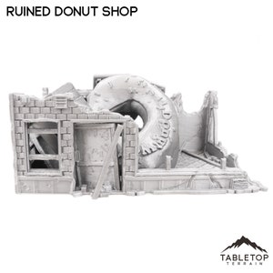 Puede incluir: Un modelo impreso en 3D gris de una tienda de donas en ruinas con una gran llanta de dona en el medio del edificio. El edificio está hecho de ladrillo y tiene una ventana en el lateral. La llanta de dona tiene la palabra "Donut" escrita en ella.