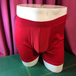 May include: Red boxer briefs on a white mannequin. The underwear has a smooth, seamless design.