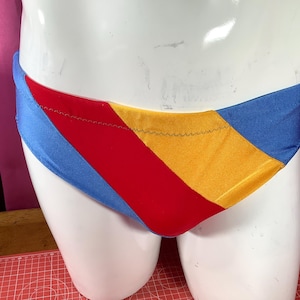 May include: A blue, red, and yellow striped swimsuit with a contrasting white seam.