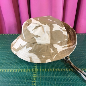 May include: A camouflage-patterned bucket hat with a brown and white color scheme. The hat has a drawstring and a cord.