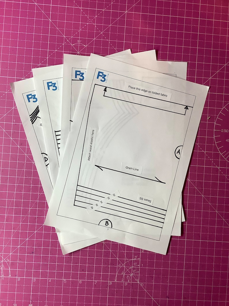 Puede incluir: Cuatro hojas de papel blancas con el texto "F3" impreso en ellas. La hoja superior tiene instrucciones para coser, incluyendo "Place this edge on folded fabric", "Grain Line", "Seam SS" y "Attach waist elastic here".
