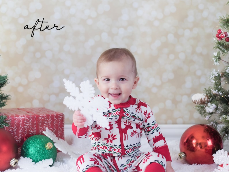 May include: A baby in a red and white Christmas pajamas holds a white snowflake ornament. The baby is sitting on a white fluffy surface with red and green Christmas ornaments and a wrapped gift box.