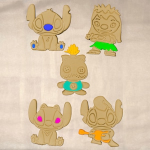 May include: Five tan-colored character cookie cutters with colorful accents. The characters include Stitch, Lilo, and other figures from the Lilo & Stitch franchise. The cutters have blue, green, yellow, and pink details.