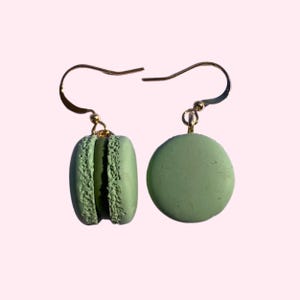 Könnte beinhalten: Ein Paar grüne Makronen-Ohrringe mit goldenen Haken. Die Makronen sind aus Polymer Clay gefertigt und haben eine realistische Textur.