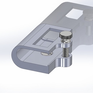 May include: A silver metal clamp with a threaded screw and a knob. The clamp is designed to hold two pieces of material together.