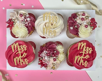 Può includere: Sei cupcake decorati con glitter dorati e codette. I cupcake sono disposti in un portacupcake bianco. I cupcake sono decorati con le parole "Miss to Mrs".