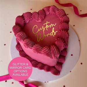 May include: A heart-shaped cake with pink frosting and a gold inscription that reads "Custom Words".