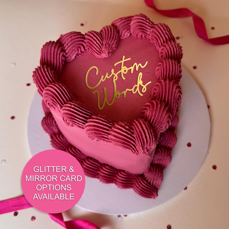 May include: A heart-shaped cake with pink frosting and a gold inscription that reads "Custom Words".