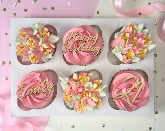 May include: Six pink cupcakes with gold glitter frosting and gold glitter lettering. The cupcakes are arranged in a white box. The cupcakes are decorated with the words "Happy Birthday", "Emily", and the number "21".