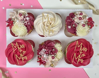 Può includere: Sei cupcake decorati con glassa bianca e bordeaux, codette dorate e scritte dorate che dicono "Miss to Mrs". I cupcake sono disposti in una scatola di cartone bianca.