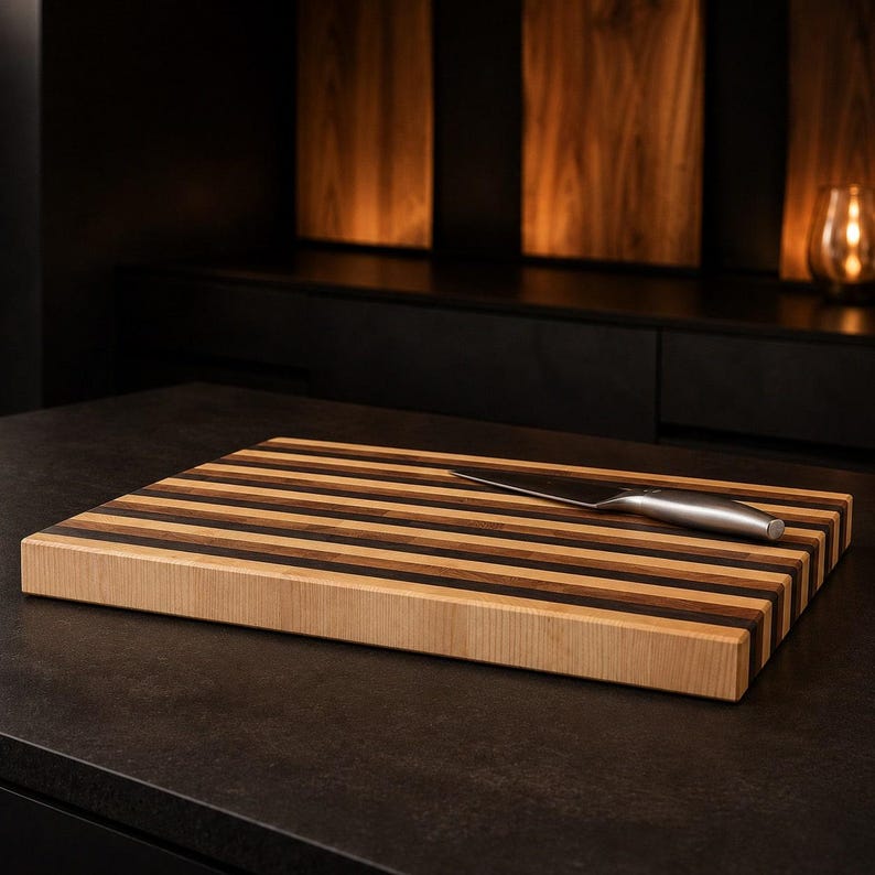 Peut inclure: Une planche &agrave; d&eacute;couper rectangulaire en bois pr&eacute;sentant des rayures horizontales altern&eacute;es de tons bois clair, moyen et fonc&eacute;. Un couteau de cuisine en acier inoxydable avec un manche argent&eacute; repose en diagonale sur la surface.