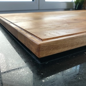 May include: A large, rectangular wooden cutting board with a thick, dark brown border. The board has a smooth, polished surface and is made of natural wood.