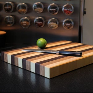 Peut inclure: Une planche &agrave; d&eacute;couper rectangulaire en bois pr&eacute;sentant des bandes verticales altern&eacute;es dans des tons de bois clair, moyen et fonc&eacute;. Un couteau de cuisine en acier inoxydable &agrave; manche noir repose horizontalement sur la planche pr&egrave;s d'un citron vert.