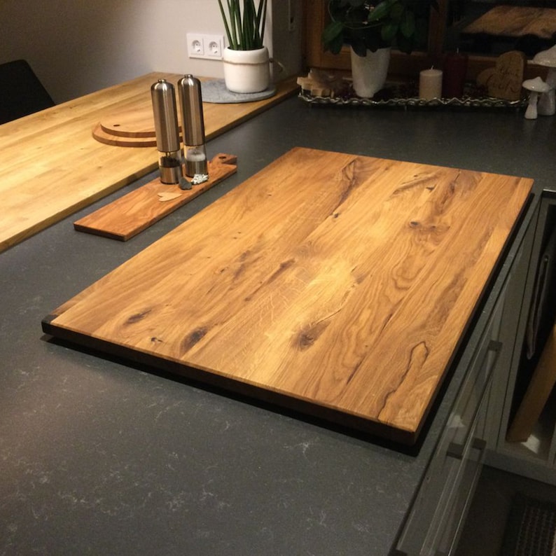 May include: A large, rectangular wooden cutting board with a dark brown border. The board has a natural wood grain pattern and is made of oak.