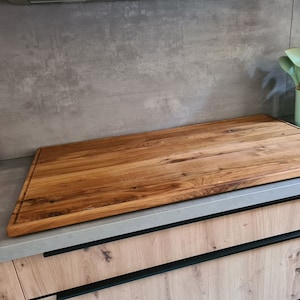 May include: A large, rectangular wooden cutting board with a natural wood finish. The board is made of multiple pieces of wood that have been joined together. The board is sitting on a countertop.