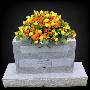 This Large Headstone Saddle has grave flowers including Orange Mix Mini-Mums. It is a funeral or memorial decoration.