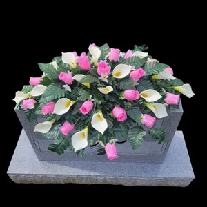 This Headstone Saddle has silk grave flowers including Pink Rosebuds and Cream Calla Lilies. It is a funeral or cemetery decoration.