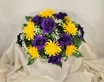 This headstone saddle has grave flowers including purple open roses and yellow spider mums. It is a funeral or memorial decoration.