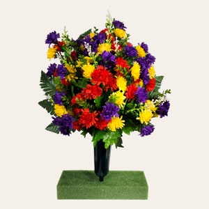 May include: A colorful artificial flower arrangement in a black vase with a green foam base. The arrangement features red, yellow, and purple flowers.