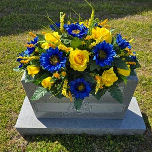 This headstone saddle includes Blue Sunflowers and Yellow Elegant Roses.  It is a memorial decoration.