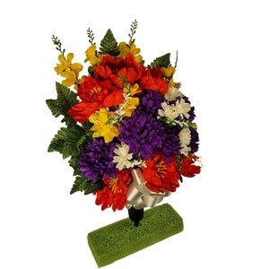 This Jumbo cemetery cone has grave flowers including Red Peonies, Purple Mums, & Yellow Delphiniums and comes with a waterproof white bow.