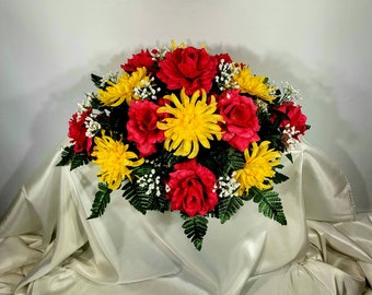 This headstone saddle has grave flowers including red open roses and yellow spider mums. It is a funeral or memorial decoration.